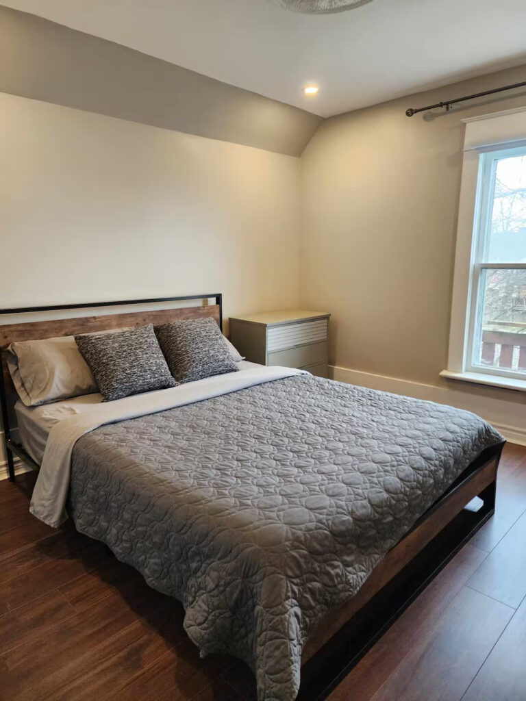 Furnished bedroom with a queen bed and grey bedding in a Niagara Falls monthly rental